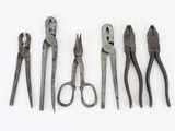 five pairs of pliers and a pair of scissors on a white surface