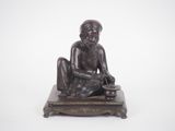 bronze statue of a man sitting on a platform with a knife in his hand