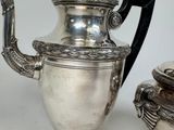 a silver tea pot with a black handle next to a silver tea pot