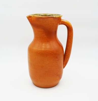 a small orange pitcher with a handle on a white surface