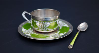 une tasse et une cuillère en argent posées sur une assiette verte