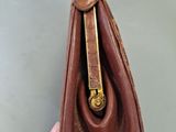 a hand holding a brown purse with a gold handle