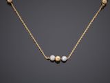 a gold necklace with three pearls on a black background