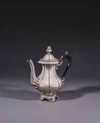 a silver teapot with a black handle on a gray surface