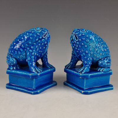 une paire de figurines de grenouilles en céramique bleue posées sur des socles, sur fond gris