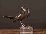 bronze sculpture of a bird on a clear base on a wooden table