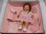 une poupée dans une boîte rose, avec des vêtements et une tétine