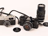 two cameras sitting next to each other on a white surface