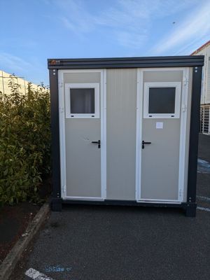des toilettes portables installées sur un parking, à côté d'un buisson