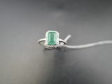 Une bague sertie d'une émeraude et de diamants repose sur une table, à côté d'une souris d'ordinateur