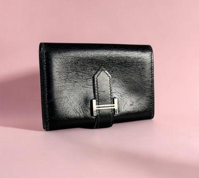 a black leather wallet with a metal clasp on a pink background