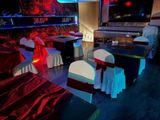 Des tables et des chaises, recouvertes de nappes rouges et blanches, sont disposées dans une pièce faiblement éclairée.