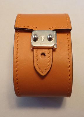 un bracelet en cuir orange muni d'un fermoir métallique, posé sur un fond blanc