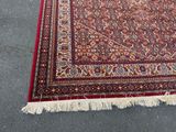 un tapis oriental avec une bordure rouge et des franges, posé sur le sol