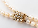 two strands of pearls with a gold clasp on a white surface