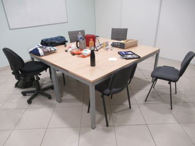 une table avec des chaises et un ordinateur portable posé dessus, dans une pièce