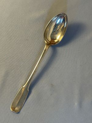 silver plated spoon on a white tablecloth with a shadow on the surface