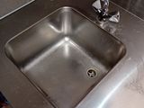 a stainless steel sink in the corner of a bathroom