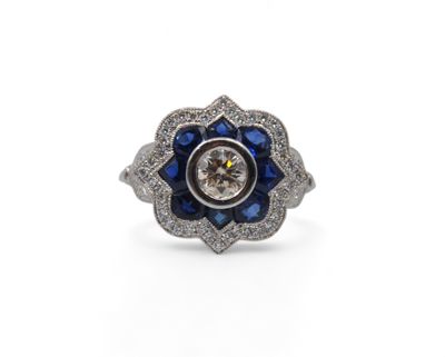 un gros plan d'une bague ornée d'une fleur en diamants et saphirs sur fond blanc