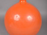 un vase orange posé sur une surface grise