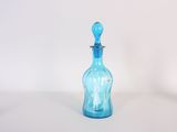 une bouteille en verre bleue munie d'une anse, posée sur une surface blanche