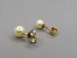 une paire de boucles d'oreilles en perles et en or posées sur un fond gris