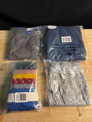 quatre paires de pantalons pour homme dans des sacs en plastique, posées sur une table en bois