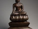 a bronze figure of a seated buddha on a lotus