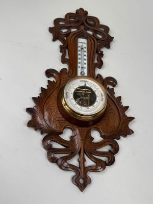 une horloge en bois accrochée au mur, sur laquelle se trouve un thermomètre