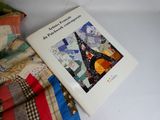 a book that is sitting on a bed next to a pile of quilts
