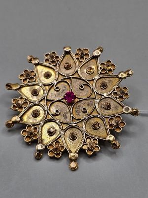 un gros plan d'une broche en or sertie d'une pierre rouge