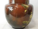a brown vase with leaves on it sitting on a table