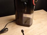 a black coffee maker on a wooden table with a red handle
