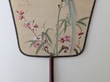 a fan with a bird painted on it hanging on a wall