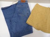 two pairs of blue jeans and a yellow sweater on a white table