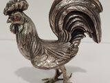 une figurine de coq en argent posée sur un fond blanc