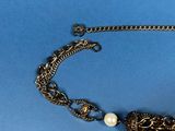a close up of a necklace with a chain and a pearl