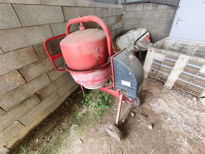 a red cement mixer sitting next to a brick wall