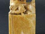 une figurine ancienne sculptée représentant un chien, posée sur un socle
