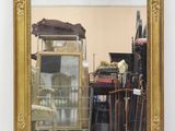 a gold framed mirror sitting on the floor in front of a chair
