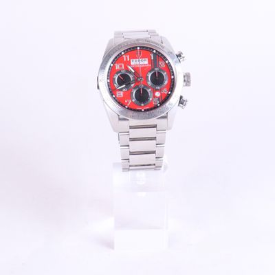 une montre en argent au cadran rouge posée sur un socle transparent