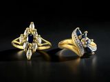 two gold rings with diamonds and sapphires on a black background