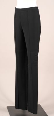 La femme porte un haut blanc et un pantalon noir.