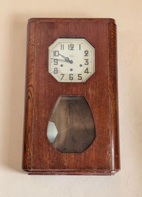 une horloge en bois accrochée au mur à côté d'un vase