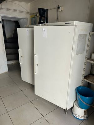 two white refrigerators in a room with a blue bucket on the floor