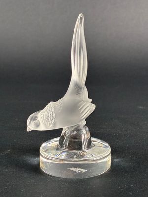 figurine d'oiseau en verre transparent posée sur un socle transparent, sur une surface noire