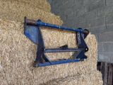 une botte de foin à laquelle est fixée une charrue bleue, dans une grange