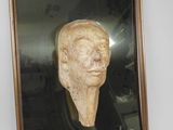 tableau représentant la tête d'un homme, dans un cadre doré, accroché à un mur blanc