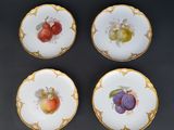 four plates with fruit painted on them sitting on a table