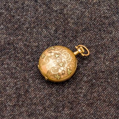 une petite montre de poche en or posée sur un tissu gris